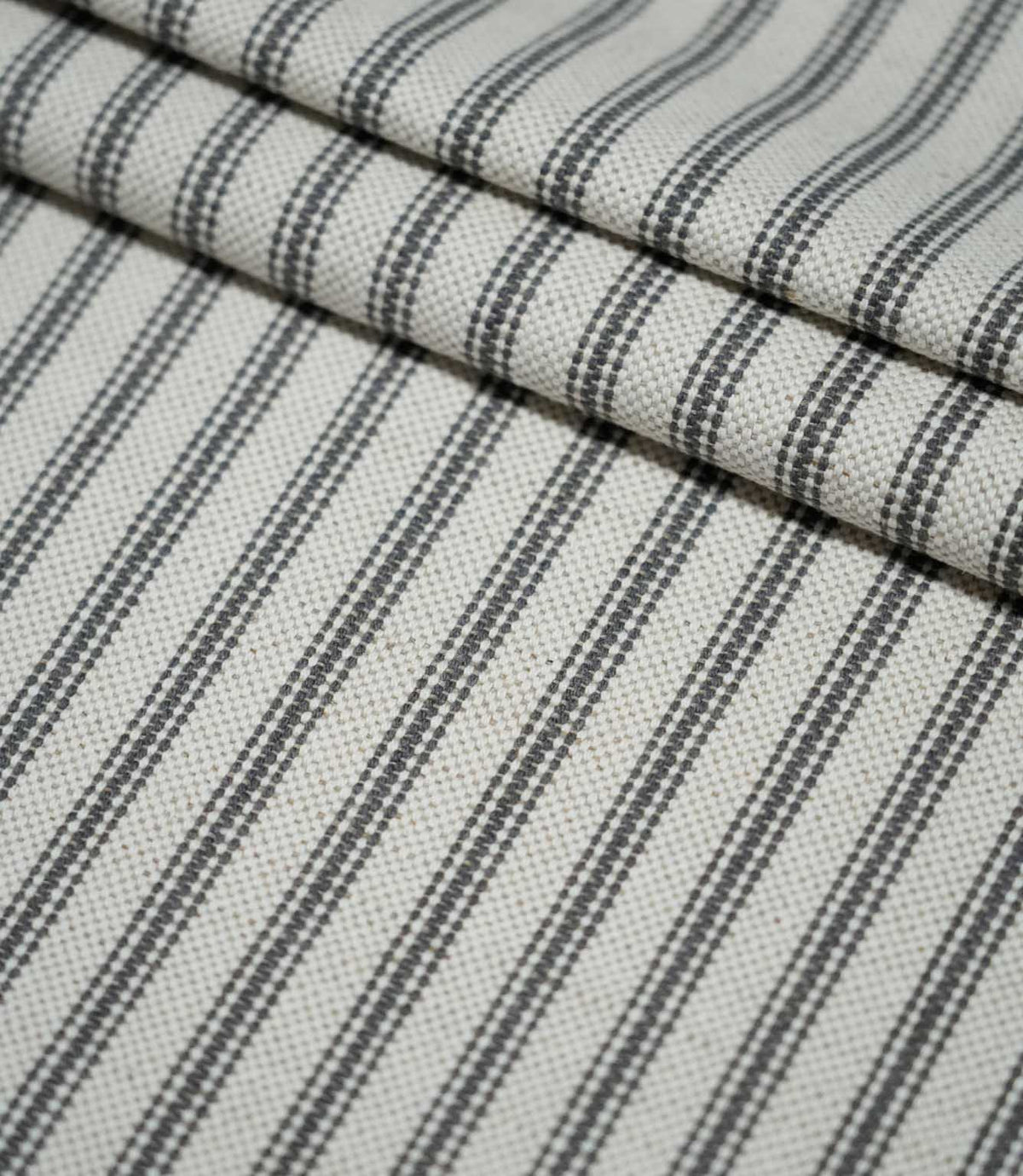 Layered folds of grey ticking stripe fabric, highlighting the evenly spaced charcoal stripes and tactile woven texture.