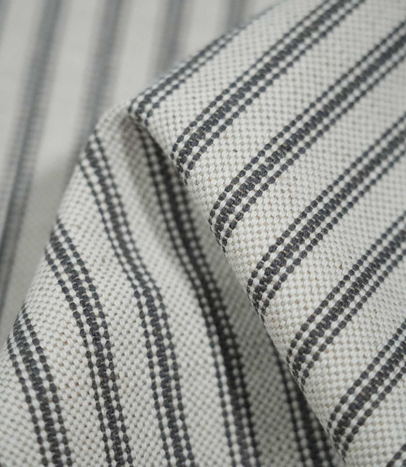 Detailed close-up of folded grey ticking stripe fabric showing the charcoal grey woven stripes against a natural cream textured background.