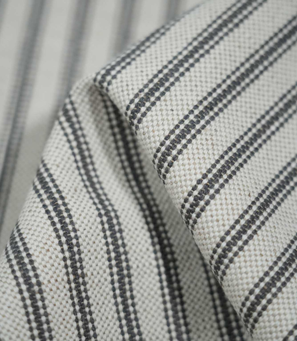 Detailed close-up of folded grey ticking stripe fabric showing the charcoal grey woven stripes against a natural cream textured background.