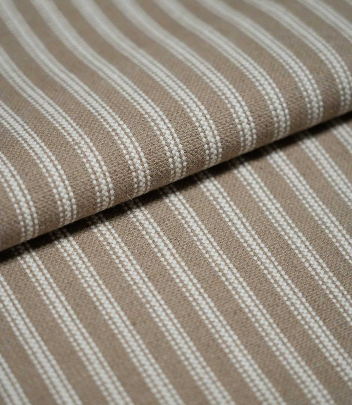 Folded natural ticking stripe fabric showing the repeating ivory striped design and textured taupe-beige woven finish.