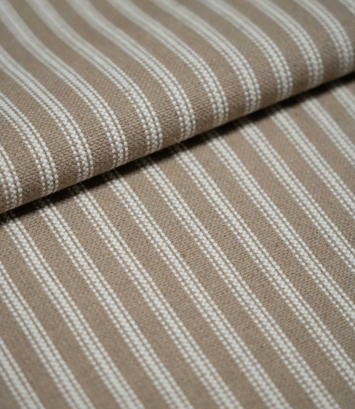 Close-up of natural ticking stripe fabric arranged in a soft fold, highlighting the fine ivory stripes and subtle woven texture.