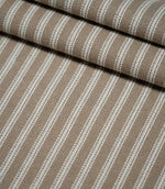Layered folds of natural ticking stripe fabric with repeating ivory stripes, showing the texture and structure of the warm taupe woven fabric.