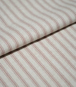 Folded pink ticking stripe fabric showing the repeating dusty pink striped design and softly textured cream woven background.