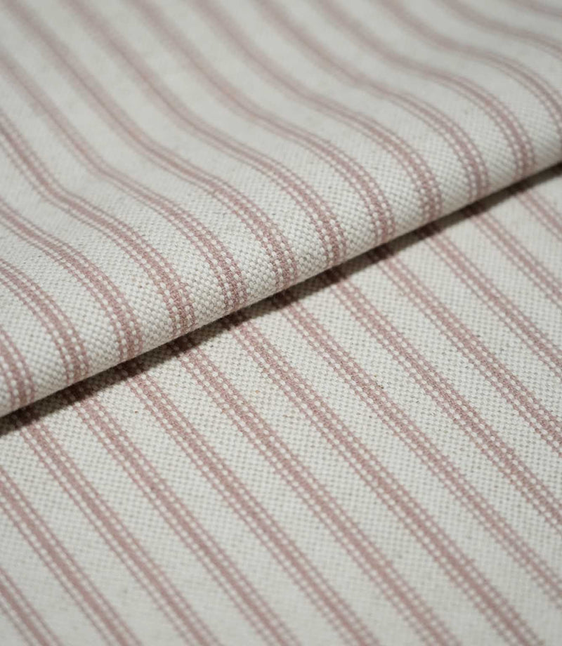 Folded pink ticking stripe fabric showing the repeating dusty pink striped design and softly textured cream woven background.