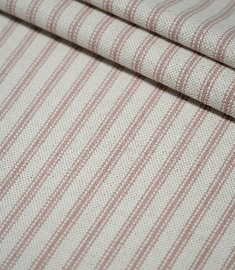 Layered folds of pink ticking stripe fabric with narrow dusty pink woven stripes on a cream background, highlighting the fabric’s texture and repeating pattern.