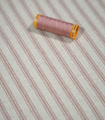 Pink ticking stripe fabric with a coordinating dusty pink thread spool, showing the fine striped pattern and textured cream weave in close detail.