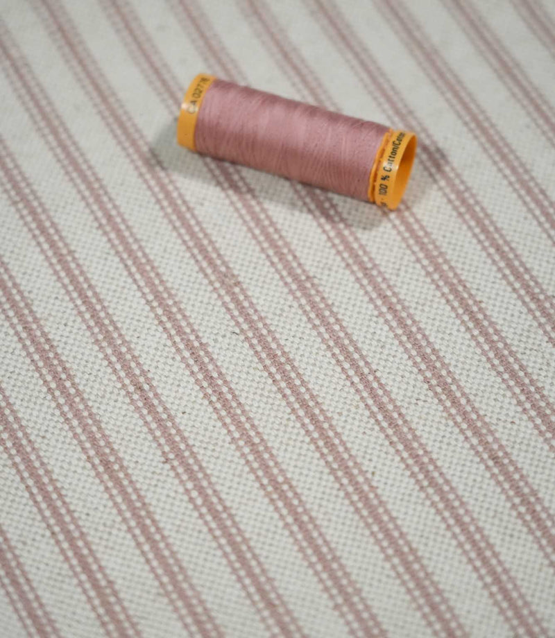 Pink ticking stripe fabric with a coordinating dusty pink thread spool, showing the fine striped pattern and textured cream weave in close detail.
