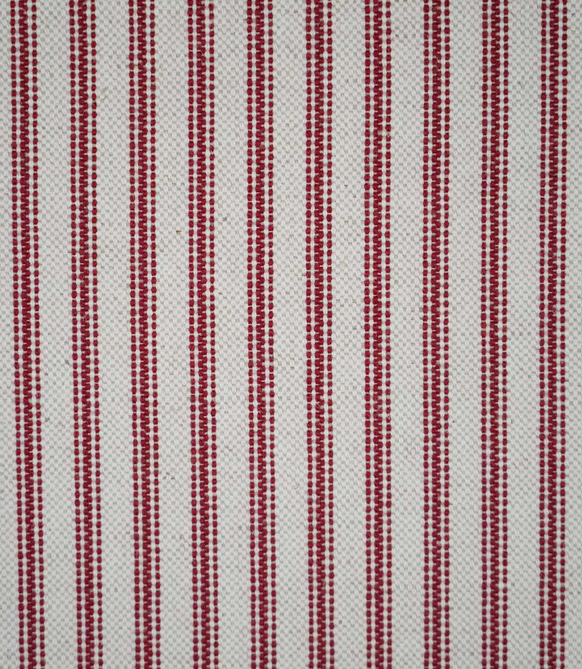 Close-up of red ticking stripe fabric featuring narrow woven red stripes on a natural cream background, highlighting the textured weave and classic striped design.