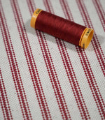 Red ticking stripe fabric with a coordinating red thread spool, highlighting the rich red stripes and textured natural cream woven background.