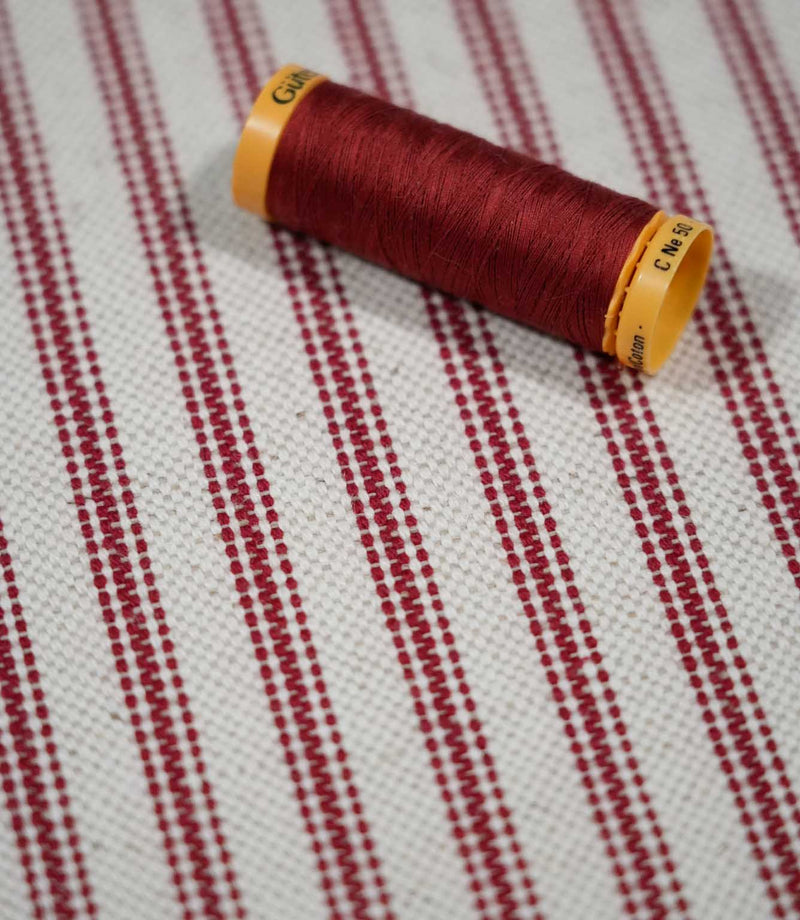 Red ticking stripe fabric with a coordinating red thread spool, highlighting the rich red stripes and textured natural cream woven background.