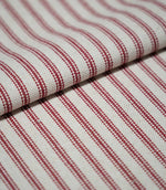 Folded red ticking stripe fabric showing the repeating narrow red stripes and textured cream weave in close detail.