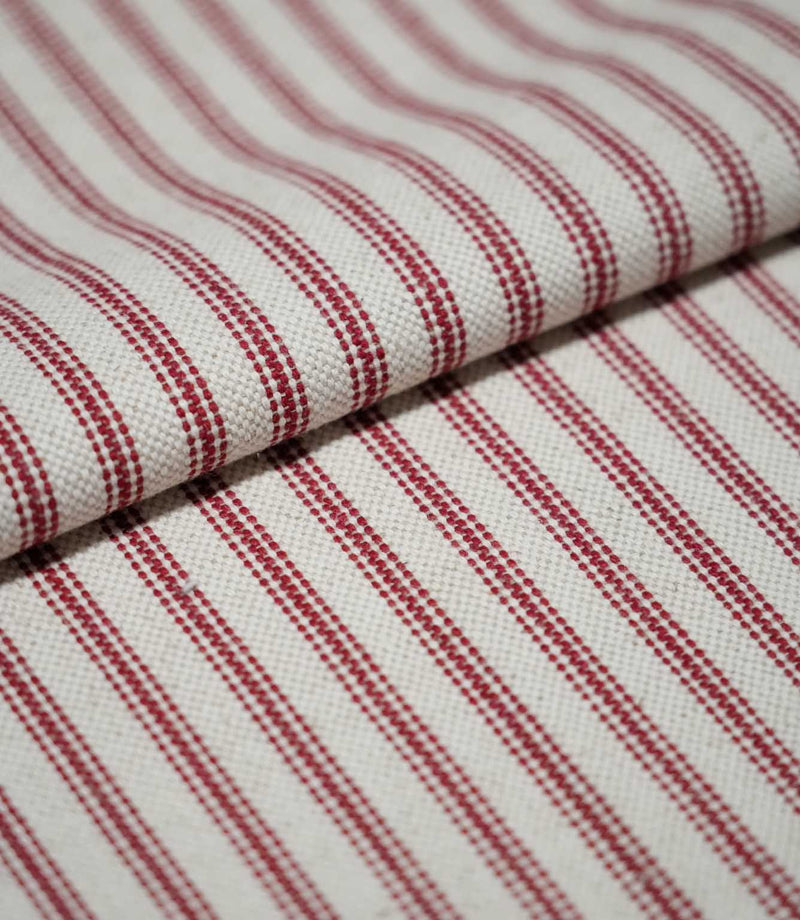 Folded red ticking stripe fabric showing the repeating narrow red stripes and textured cream weave in close detail.