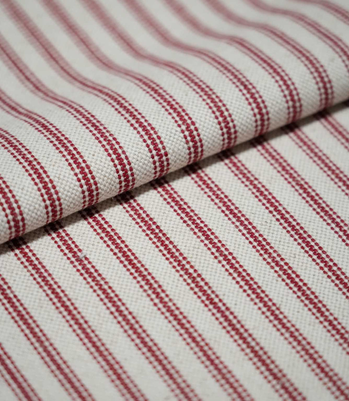 Folded red ticking stripe fabric showing the repeating narrow red stripes and textured cream weave in close detail.