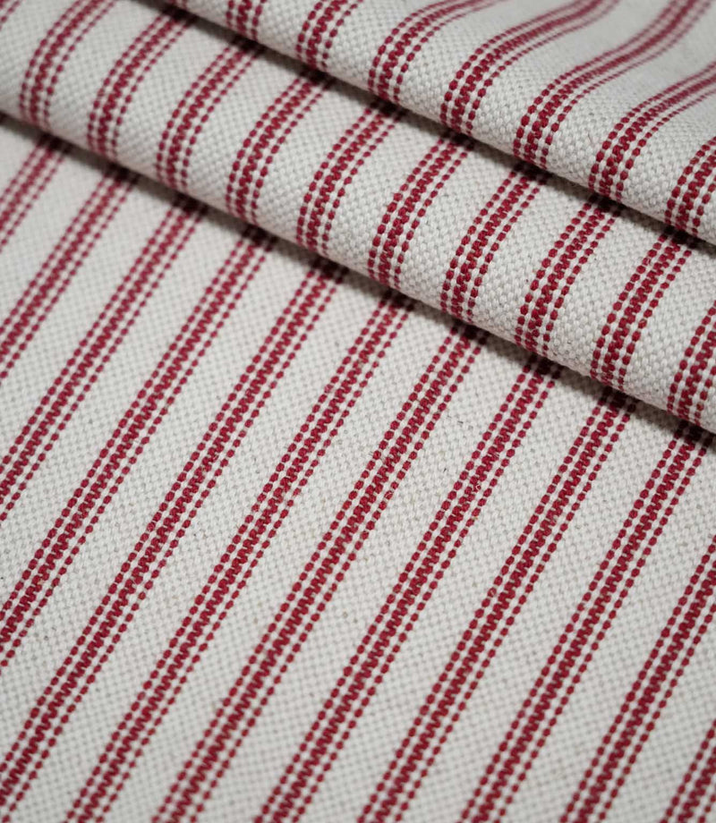 Layered folds of red ticking stripe fabric with evenly spaced red woven stripes on a natural cream background, highlighting the fabric texture and pattern.