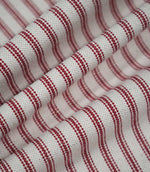 Red ticking stripe fabric arranged in soft flowing folds, showing the rich red woven stripes, natural cream ground and textured finish.