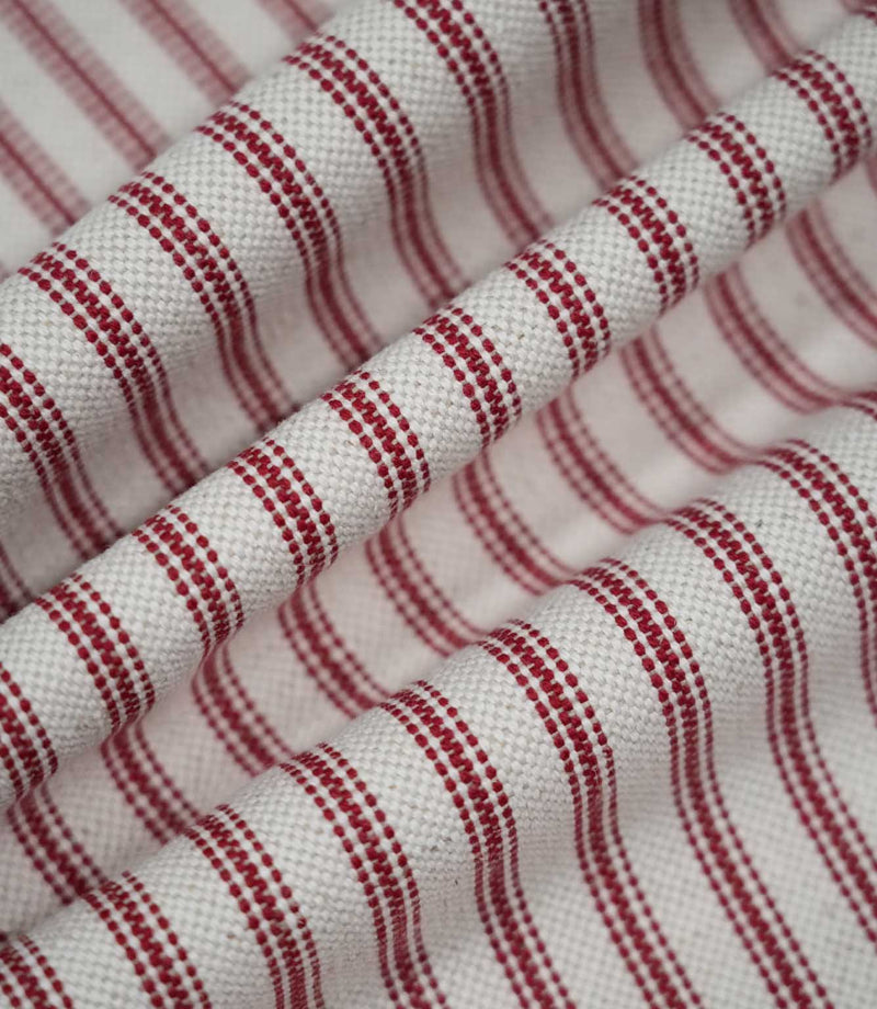 Red ticking stripe fabric arranged in soft flowing folds, showing the rich red woven stripes, natural cream ground and textured finish.
