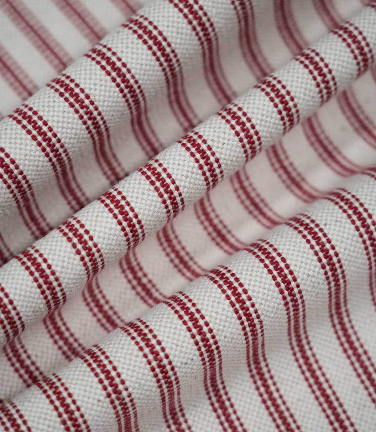 Red ticking stripe fabric arranged in soft flowing folds, showing the rich red woven stripes, natural cream ground and textured finish.