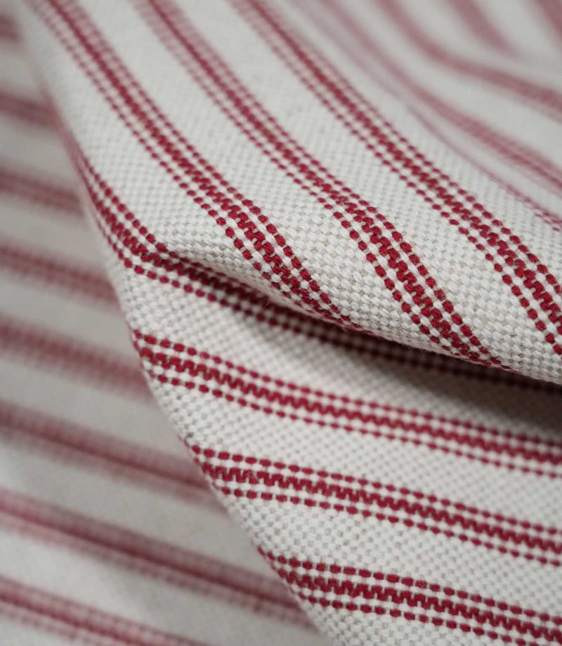 Detailed close-up of draped red ticking stripe fabric, highlighting the narrow red stripes, natural cream woven background and tactile textured weave.