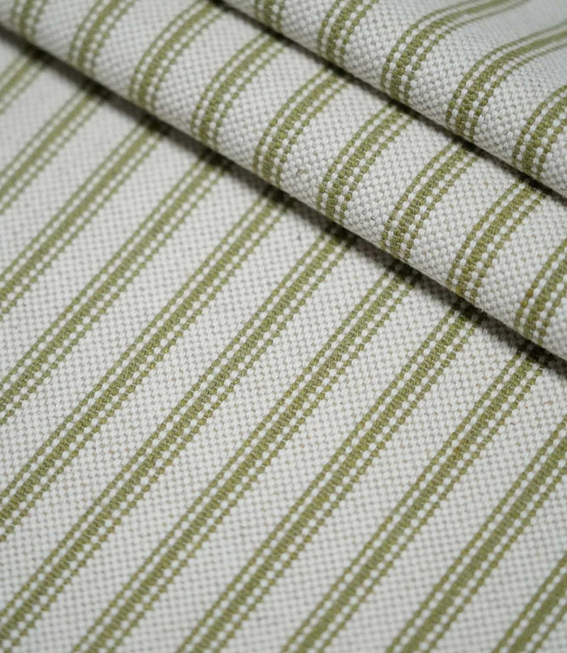 Layered folds of sage green ticking stripe fabric with evenly spaced woven stripes on a natural cream background, highlighting the fabric texture and pattern.