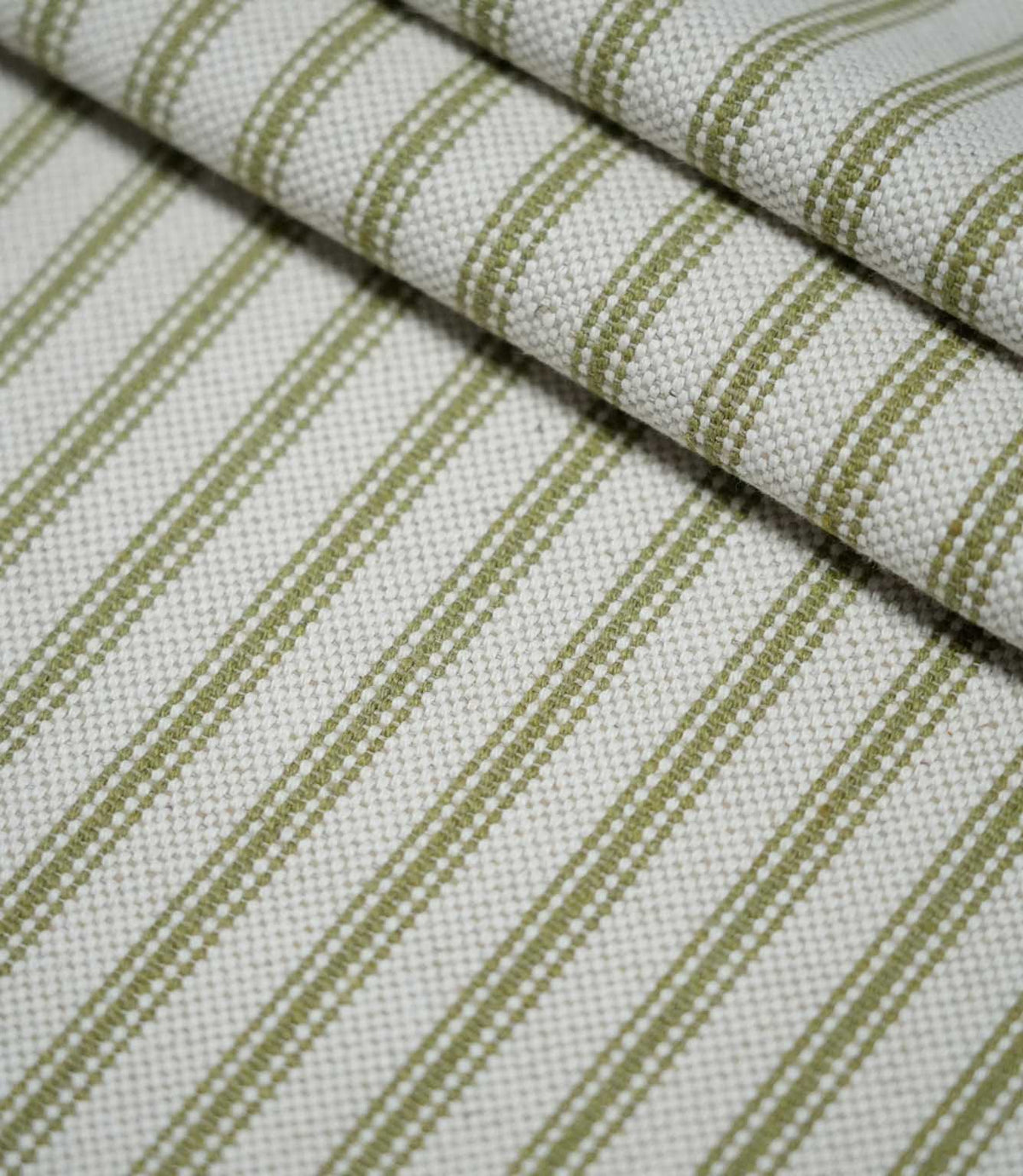 Layered folds of sage green ticking stripe fabric with evenly spaced woven stripes on a natural cream background, highlighting the fabric texture and pattern.