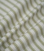 Sage green ticking stripe fabric arranged in soft flowing folds, showing the repeating green stripes, natural cream ground and textured woven finish.