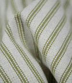 Detailed close-up of draped sage green ticking stripe fabric, highlighting the narrow woven stripes, natural cream background and tactile textured weave.