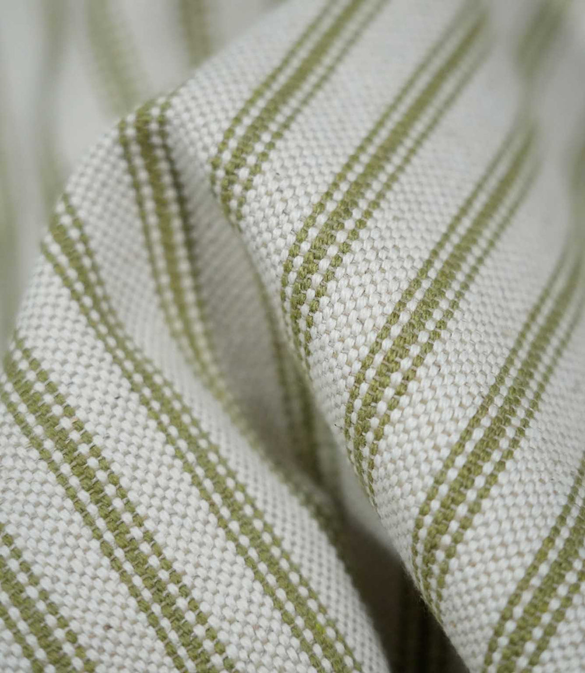 Detailed close-up of draped sage green ticking stripe fabric, highlighting the narrow woven stripes, natural cream background and tactile textured weave.