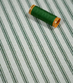 Sap green ticking stripe fabric with a coordinating green thread spool, highlighting the narrow striped pattern and textured natural cream weave.