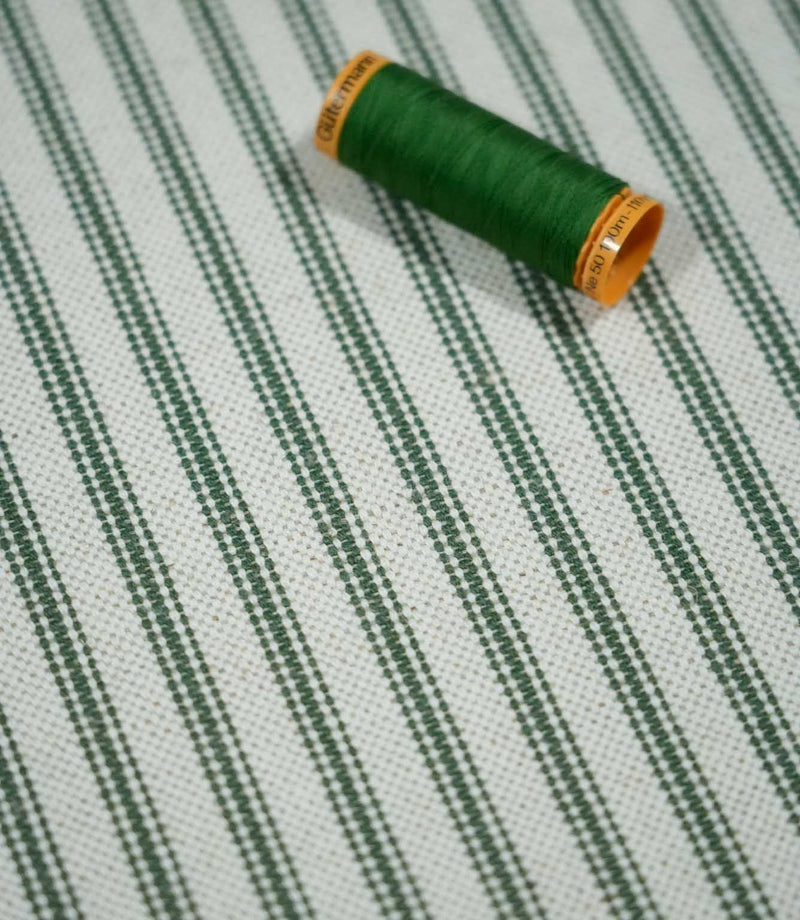Sap green ticking stripe fabric with a coordinating green thread spool, highlighting the narrow striped pattern and textured natural cream weave.
