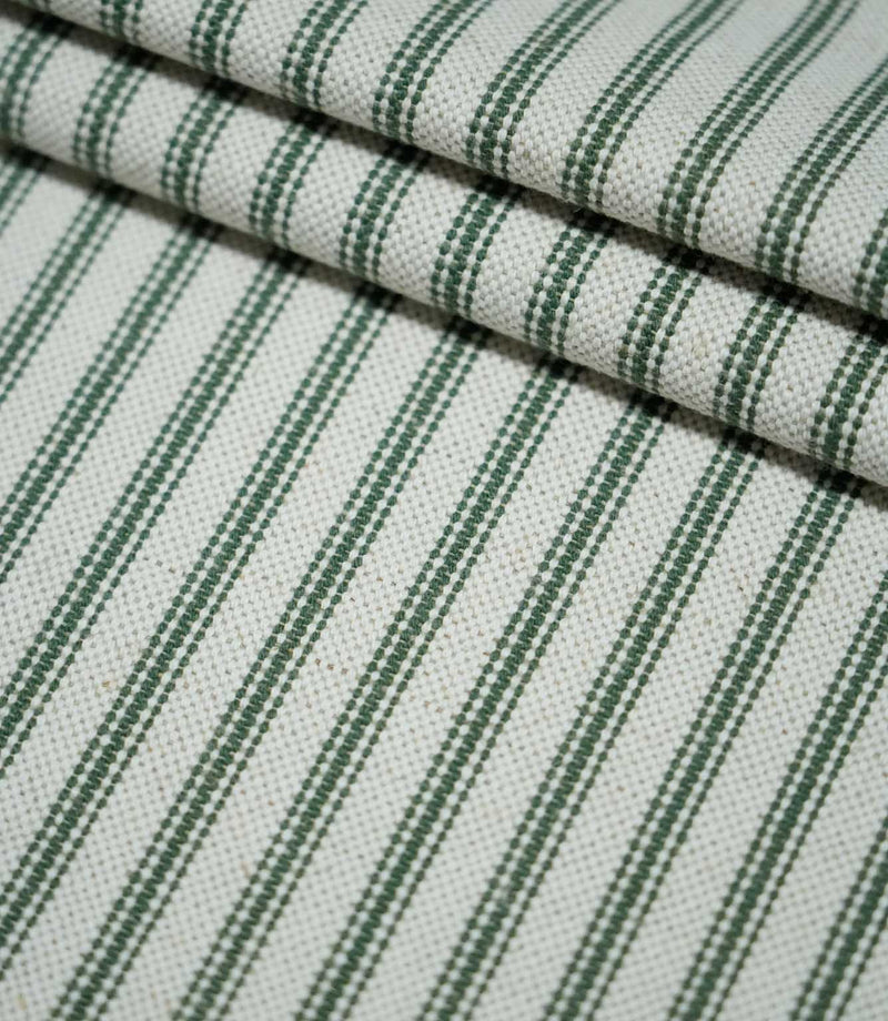 Layered folds of sap green ticking stripe fabric with evenly spaced dark green stripes on a natural cream background, highlighting the woven texture.