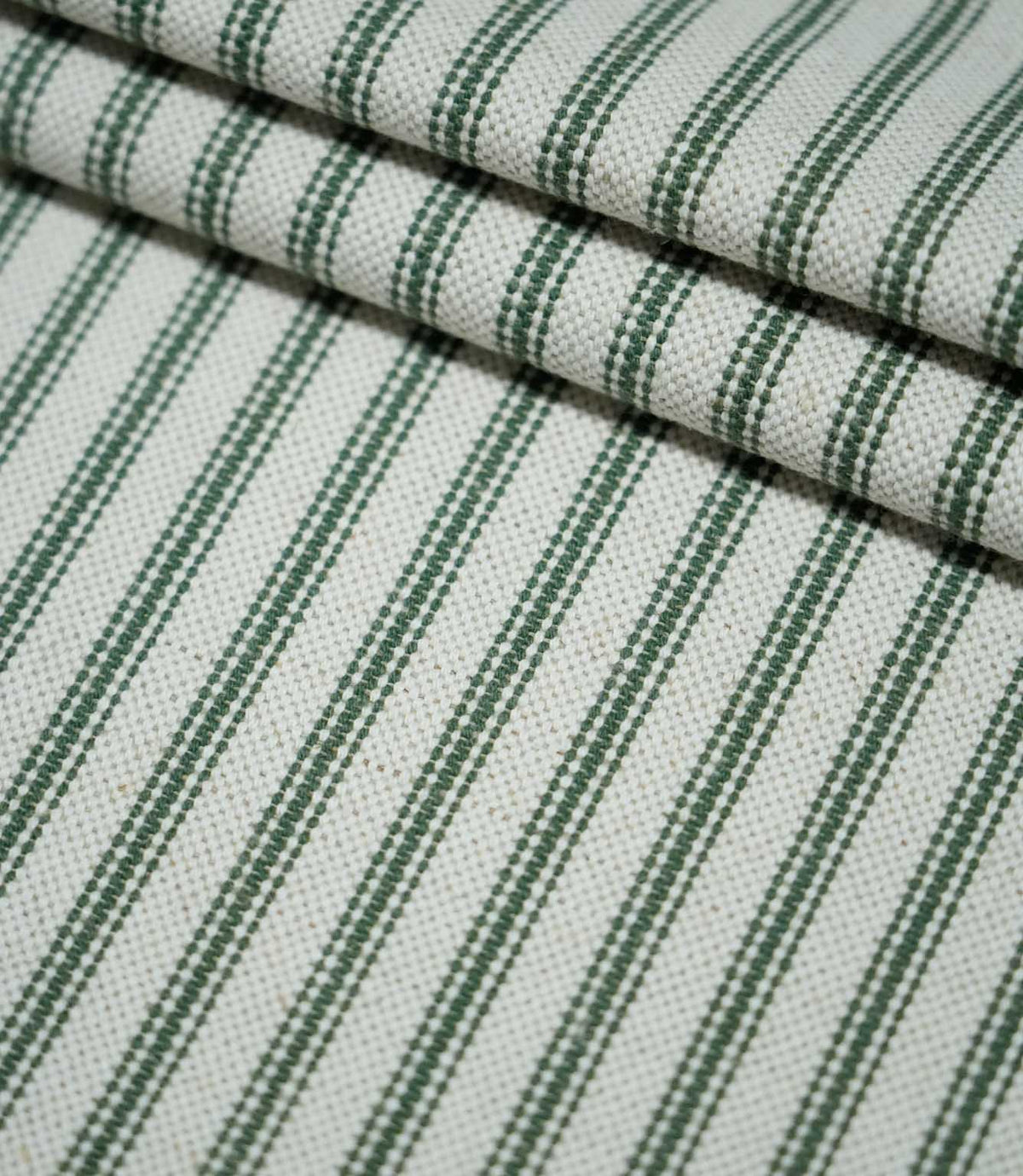 Layered folds of sap green ticking stripe fabric with evenly spaced dark green stripes on a natural cream background, highlighting the woven texture.