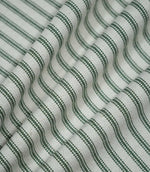 Sap green ticking stripe fabric arranged in soft flowing folds, showing the repeating dark green stripes, natural cream ground and tactile woven finish.