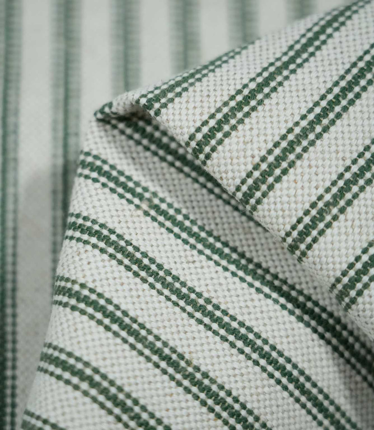 Detailed close-up of folded sap green ticking stripe fabric, highlighting the dark green woven stripes, natural cream background and textured weave.