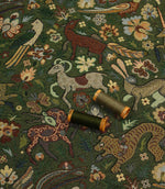 Decorative tapestry fabric with animal and floral patterns and two spools of thread on top.