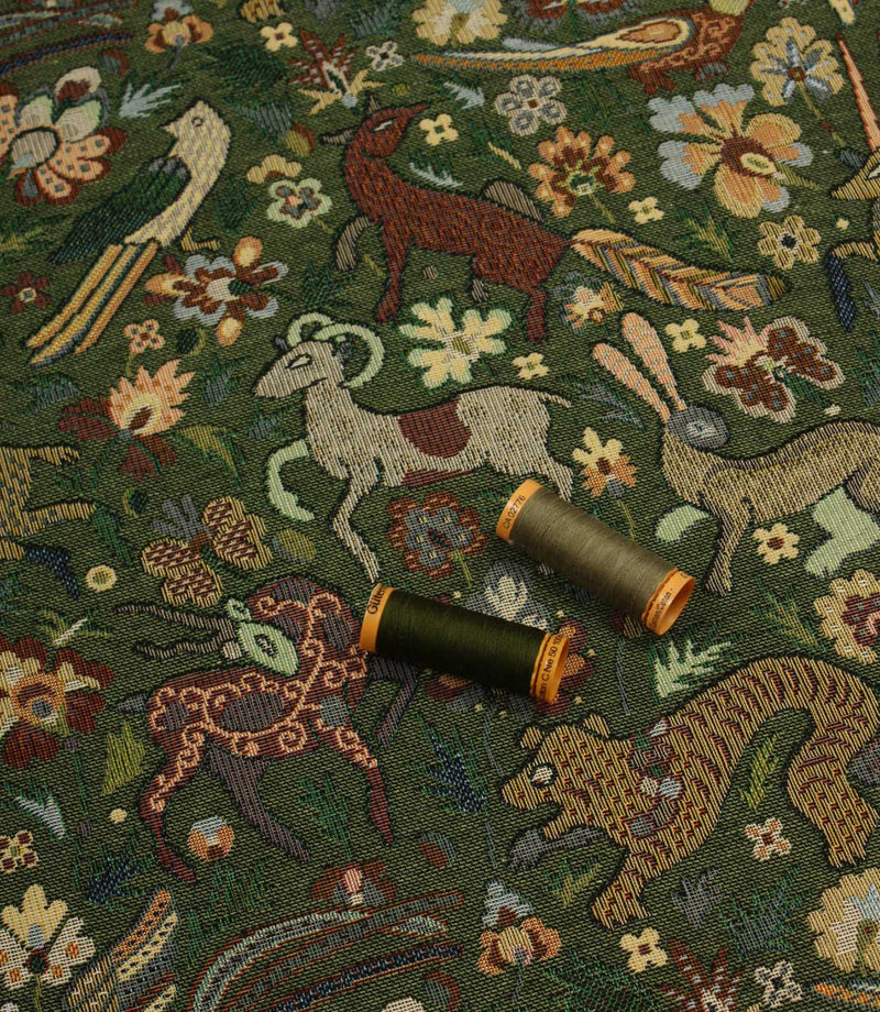 Decorative tapestry fabric with animal and floral patterns and two spools of thread on top.