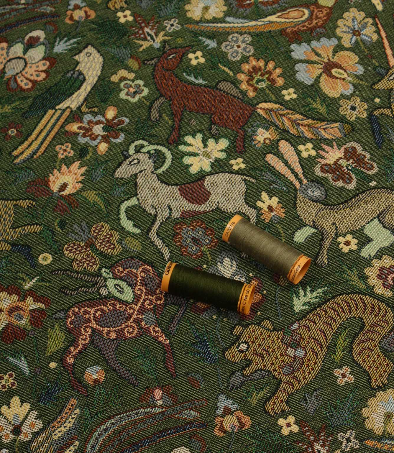 Decorative tapestry fabric with animal and floral patterns and two spools of thread on top.