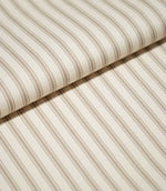 Close-up of folded JF Ticking Beige fabric showing fine beige ticking stripes and a subtle herringbone texture on a warm cream background.