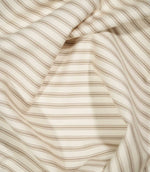 JF Ticking Beige fabric draped in soft folds, highlighting the classic beige ticking stripe design and subtle herringbone weave.