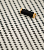JF Ticking Black fabric styled with a coordinating black thread spool, highlighting the classic stripe pattern and subtle woven herringbone texture.
