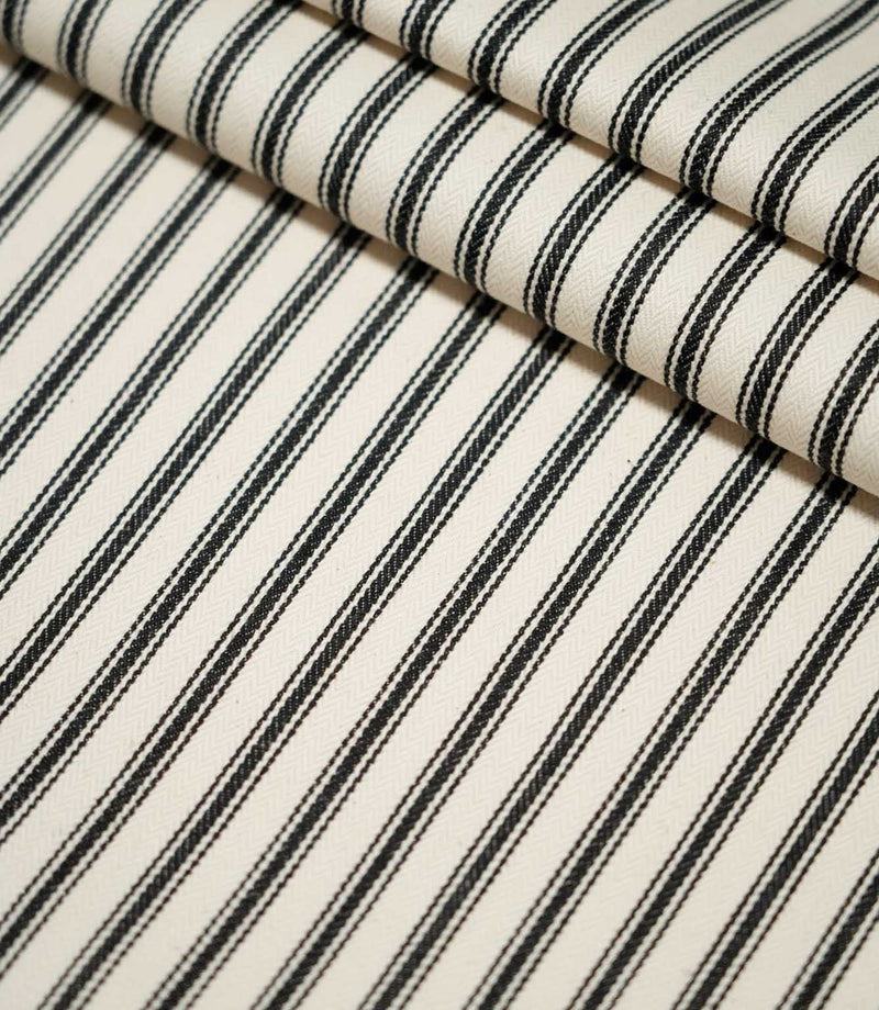 JF Ticking Black striped fabric laid flat and folded, showing the repeating black ticking stripe design and textured cream woven ground.