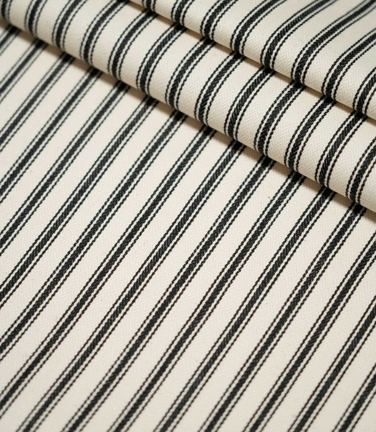JF Ticking Black striped fabric laid flat and folded, showing the repeating black ticking stripe design and textured cream woven ground.