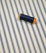 JF Ticking Blue fabric styled with a coordinating navy thread spool, highlighting the classic blue ticking stripes and cream woven ground.