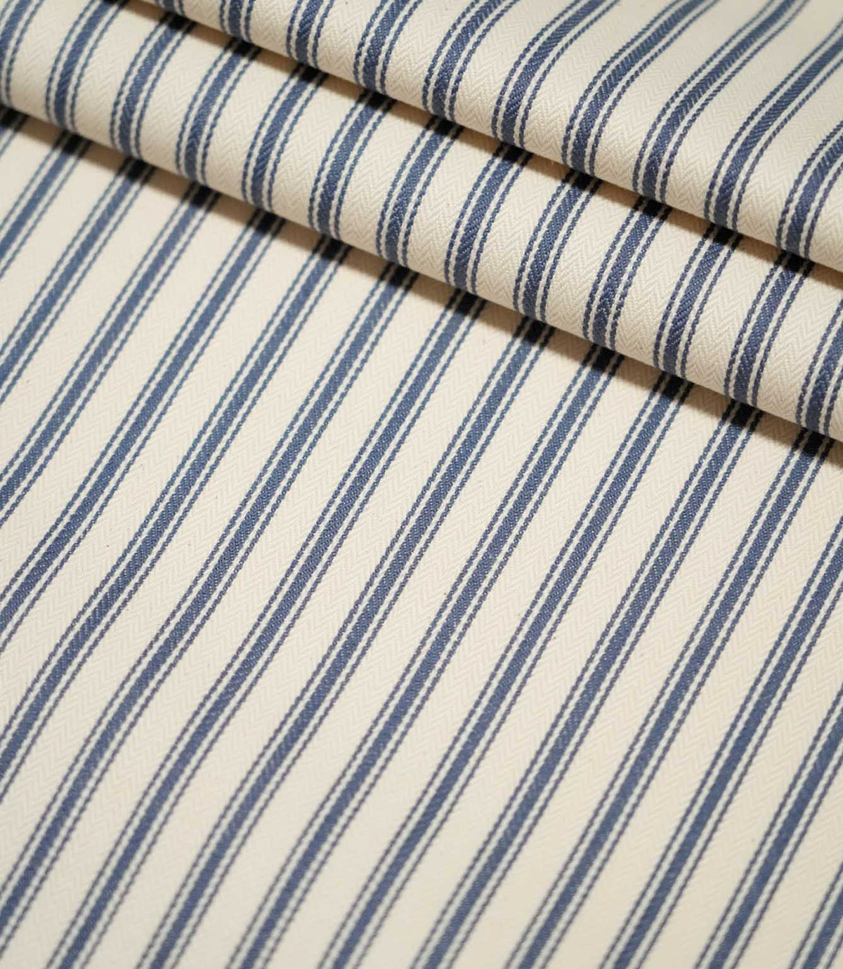 JF Ticking Blue striped fabric laid flat and neatly folded, showing the repeating blue ticking stripe design and textured cream weave.