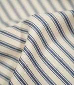 Detailed close-up of JF Ticking Blue fabric showing the blue woven ticking stripes, warm cream ground and fine herringbone texture.