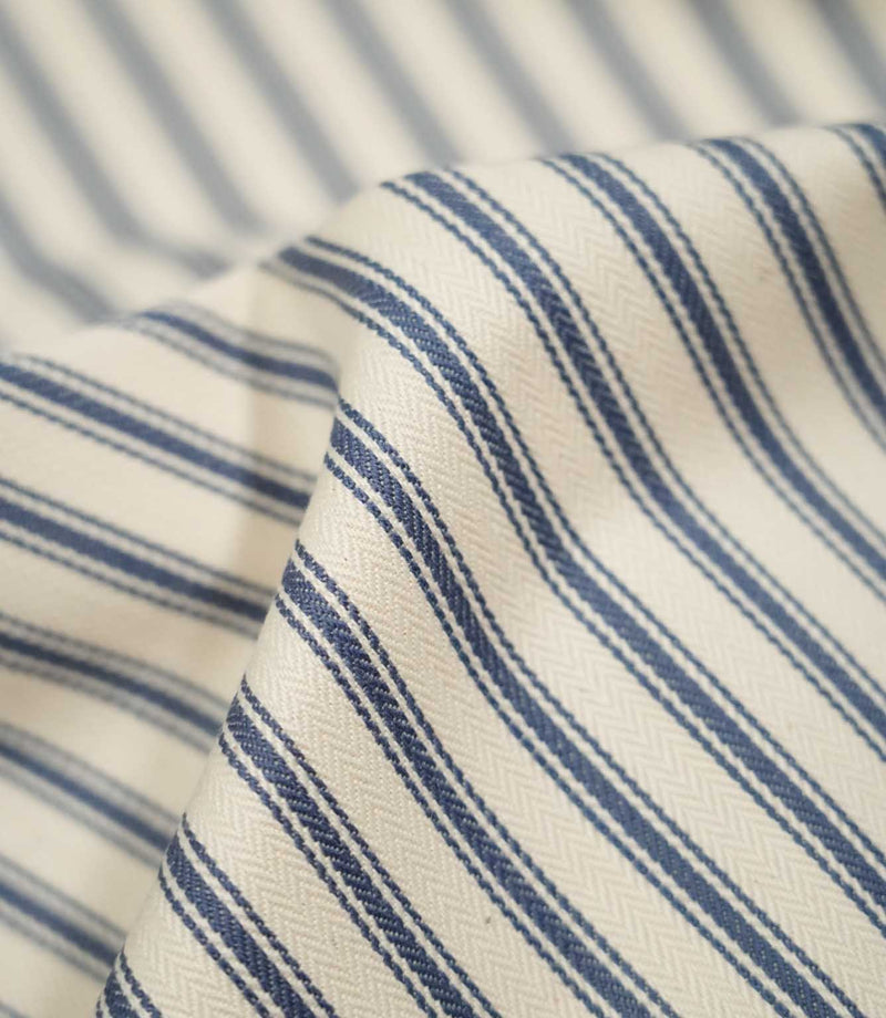 Detailed close-up of JF Ticking Blue fabric showing the blue woven ticking stripes, warm cream ground and fine herringbone texture.