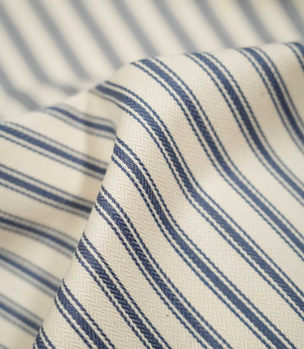 Detailed close-up of JF Ticking Blue fabric showing the blue woven ticking stripes, warm cream ground and fine herringbone texture.