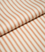 Close-up of folded JF Ticking Burnt Orange fabric showing the repeating burnt orange stripe pattern and subtle herringbone woven texture.
