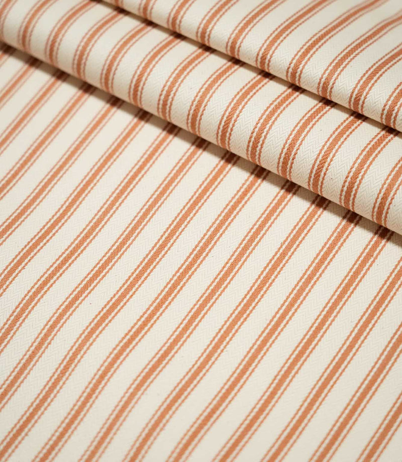 JF Ticking Burnt Orange striped fabric laid flat and neatly folded, showing the repeating ticking stripe design across a textured cream ground.