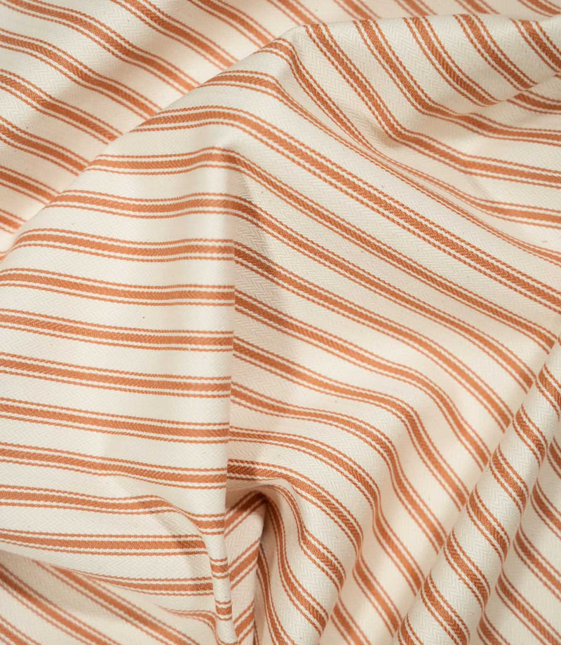 JF Ticking Burnt Orange fabric draped in soft folds, highlighting the natural drape, burnt orange ticking stripes and subtle herringbone texture.