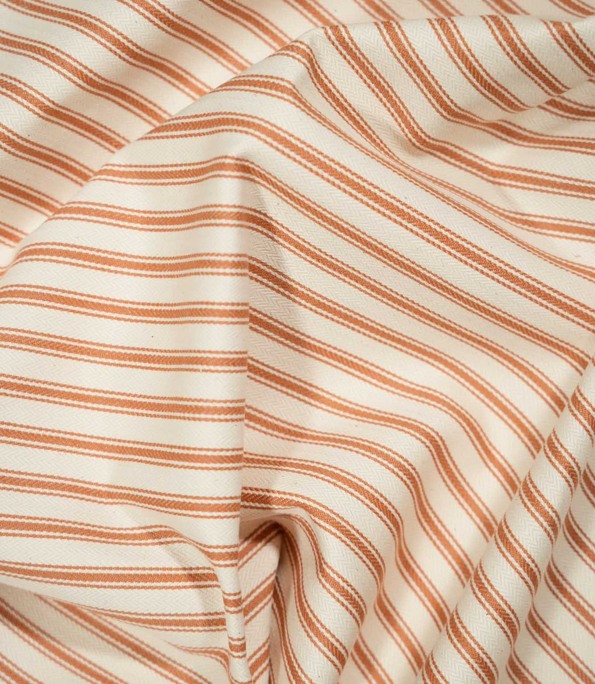 JF Ticking Burnt Orange fabric draped in soft folds, highlighting the natural drape, burnt orange ticking stripes and subtle herringbone texture.
